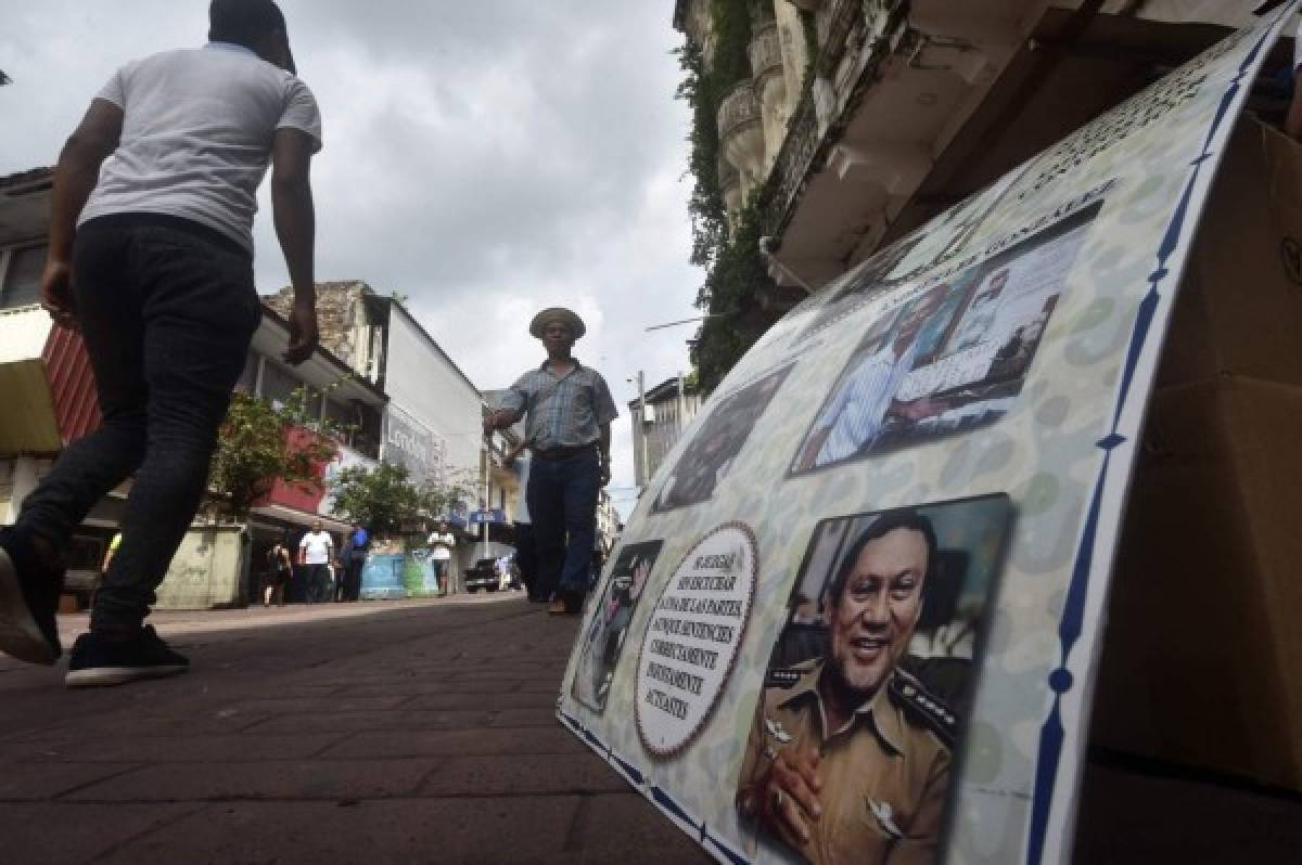 People walk past a placard with pictures of late former dictator Manuel Noriega, who became Panama's de facto ruler in 1983 and was ousted from power by US troops in 1989, in Panama City on May 31, 2017.Noriega died on late May 29 in Panama City's Santo Tomas Hospital where he had been recovering from surgery in March to remove a brain tumor, and a subsequent operation to clean up cerebral bleeding. The former dictator, who was on the CIA payroll, ousted from power by US troops in 1989, and spent years in prison for drug trafficking and money laundering, died aged 83. / AFP PHOTO / Rodrigo ARANGUA