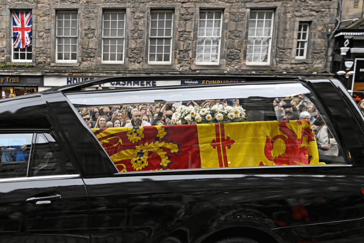 Un grupo de personas observa el coche fúnebre que lleva el ataúd de la reina Isabel II, cubierto con el estandarte real de Escocia, mientras continúa su viaje a Edimburgo desde Balmoral.