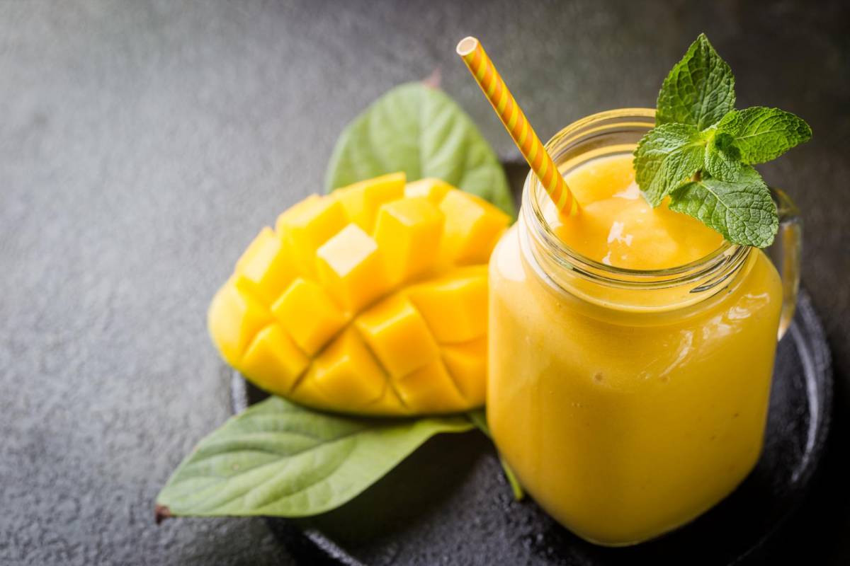 Refreshing and healthy mango smoothie in a glass with fresh fruit over stone background with copy space