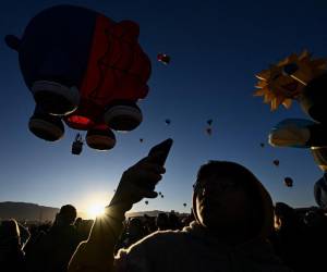 Los espectadores toman fotografías mientras el globo aerostático Spider Pig despega al amanecer durante la Fiesta Internacional de Globos de Albuquerque en Albuquerque, Nuevo México, donde están esperando observar el eclipse anular.