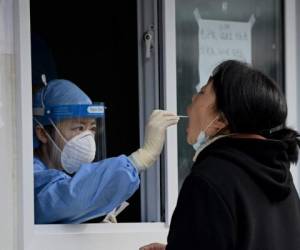 Un trabajador de la salud toma una muestra de un hisopo de una mujer para ser examinada por el coronavirus Covid-19 en Beijing el 28 de octubre de 2021. Foto: AFP