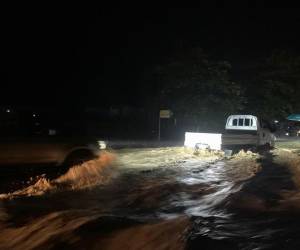 Vehículos livianos atraviesan con precaución la carretera inundada en Olanchito, una de las zonas más afectadas esta noche a causa de la tormenta tropical Sara.