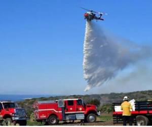 Los bomberos monitorean la situación mientras un helicóptero lanza agua a un incendio que se desató fuera de temporada en una ladera de Laguna Beach, California