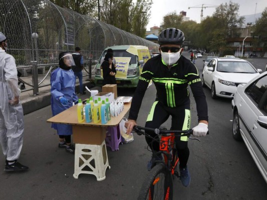 Un ciclista con mascarilla para combatir el contagio de coronavirus pasa junto a varias personas vendiendo desinfectante de manos, la escena se repite en los países en los que la gente está volviendo a su vida diaria en medio de las medidas de prevención. Foto: AP.