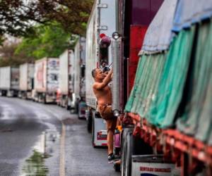 A la espera de una solución, los conductores se las ingenian para sobrevivir: duermen en los camiones entre zancudos, con riesgo de contraer dengue, compran galones de agua a los lugareños para beber y bañarse y se alimentan de comidas callejeras. AFP.