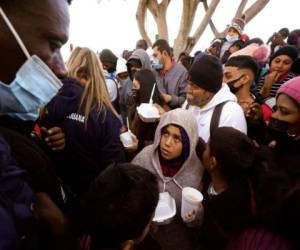 En esta fotografía de archivo del 19 de febrero de 2021, solicitantes de asilo reciben alimentos mientras esperan noticias sobre las políticas migratorias de EEUU desde la ciudad mexicana de Tijuana. (AP Foto/Gregory Bull, Archivo).