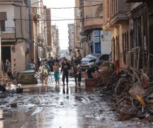 Unas personas caminan por una calle cubierta de lodo y rodeada de coches amontonados tras las intensas lluvias por la fuerte DANA, en Valencia.