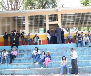 Decenas de personas esperan bajo el fuerte sol, sentados en las graderías y en algunos pupitres que las maletas electorales lleguen a los centros educativos para poder ejercer el sufragio.