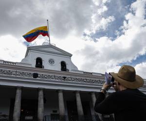 Un turista toma una foto del Palacio Presidencial de Carondelet con la bandera ecuatoriana izada hasta la mitad en honor al asesinado candidato presidencial ecuatoriano Fernando Villavicencio.