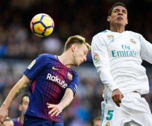 El centrocampista croata Ivan Rakitic (L) y el defensor francés Real Madrid Raphael Varane saltan por el balón durante el partido de fútbol 'Clasico' de la Liga española Real Madrid CF contra el FC Barcelona en el estadio Santiago Bernabéu en Madrid el 23 de diciembre de 2017. / AFP / JAVIER SORIANO