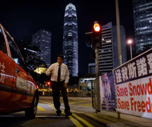 A man crosses a street next to banner displayed in support of former US spy Edward Snowden in Hong Kong on late June 17, 2013. Snowden's presence in Hong Kong is shining a global spotlight on the city, where relations with Beijing is testy, and any Chinese interference into the ongoing saga sets a precedent to how the city will be governed. AFP PHOTO / Philippe Lopez