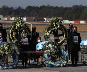 La gente espera de pie con fotografías mientras los restos de 16 migrantes guatemaltecos que fueron asesinados cerca de la frontera entre Estados Unidos y México en enero llegan a la base de la Fuerza Aérea en la Ciudad de Guatemala, el viernes 12 de marzo de 2021. (AP Foto/Moisés Castillo)