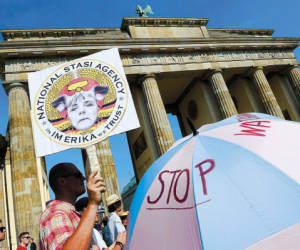 FILES - Demonstrators hold up a placard featuring German Chancellor Angela Merkel in front of Berlin's landmark Brandenburg Gate as they take part in a protest against the US National Security Agency (NSA) collecting German emails, online chats and phone calls and sharing some of it with the country's intelligence services in Berlin on July 27, 2013. Germany on October 24, 2013 summoned the US ambassador to Berlin over suspicions that Washington spied on Chancellor Angela Merkel's mobile phone, a foreign ministry spokeswoman said AFP PHOTO / JOHN MACDOUGALL