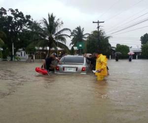 Pobladores empujan un carro en una calle inundada de Tela.