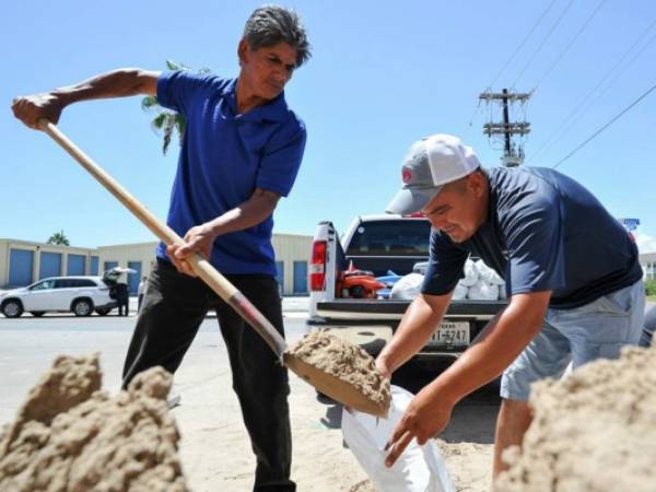 Leo Sermiento y Emilio Gutierrez, llenan sacos de arena en South Padre Island, Texas. por la posible llegada del Huracán Harvey. (Jason Hoekema/The Brownsville Herald via AP).