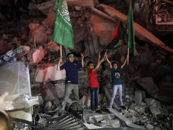 Niños palestinos ondean la bandera verde de Hamas y la palestina sobre los escombros de un edificio derribado mientras celebran el acuerdo de alto el fuego entre Israel y el grupo insurgente, en la Ciudad de Gaza. Foto:AP