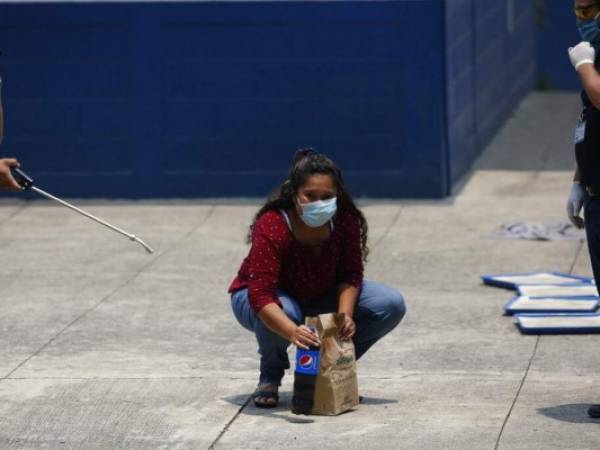 Vanessa Díaz, quien fue deportada por EEUU, recoge la comida que su madre le lleva al sitio donde los migrantes que regresan deben pasar dos semanas en cuarentena. Ya de vuelta en su casa, Díaz tiene miedo de ser agredida por vecinos. Foto: AP.