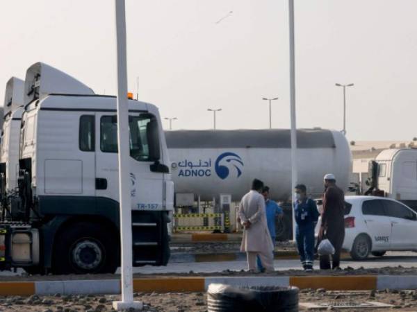 Los hombres se paran frente a una instalación de almacenamiento del gigante petrolero ADNOC en la capital de los Emiratos Árabes Unidos, Abu Dhabi, el 17 de enero de 2022. Foto: AFP