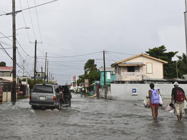 Un vehículo y peatones recorren una calle inundada debido a las fuertes lluvias antes de la llegada del huracán Lisa que ya avanza hacia el oeste de Centroamérica tras dejar lluvias en la zona insular de Honduras.