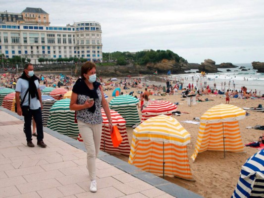 En esta fotografía de archivo del miércoles 28 de julio de 2021, dos personas que portan mascarillas para protegerse del coronavirus caminan junto a la playa en Biarritz, en el suroeste de Francia. (AP Foto/Bob Edme, archivo).