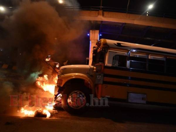 Un autobús cruza neumáticos en llamas que bloquean una carretera en Tegucigalpa. Foto: Agencia AFP.