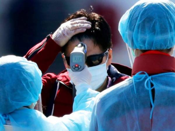 Un funcionario con traje protector toma la temperatura de los pasajeros que desembarcaron del crucero Diamond Princess, que estaba bajo cuarentena, en Yokohama, Japón. Foto: Agencia AP.