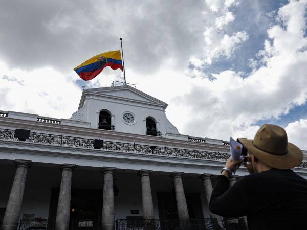 Un turista toma una foto del Palacio Presidencial de Carondelet con la bandera ecuatoriana izada hasta la mitad en honor al asesinado candidato presidencial ecuatoriano Fernando Villavicencio.