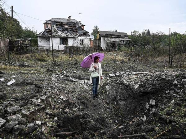 Una mujer se para frente a una casa destruida en medio de la invasión rusa de Ucrania.