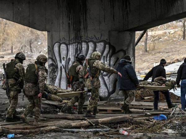 Militares ucranianos llevando cuerpos de sus compañeros en camillas en Irpin.