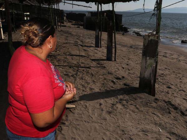 Una mujer mira el mar en la playa de Cedeño. Su casa está hecha de madera y lámina, pues ha perdido su patrimonio varias veces debido a la elevación del mar. Se resiste a irse de la zona.