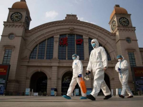 En esta imagen de archivo, tomada el 7 de abril de 2020, trabajadores vestidos con equipos de protección pasan por delante de la estación de tren de Hankou en la víspera de la reanudación de los viajes con destino en Wuhan, en la provincia de Hubei, en el centro de China. Foto: AP