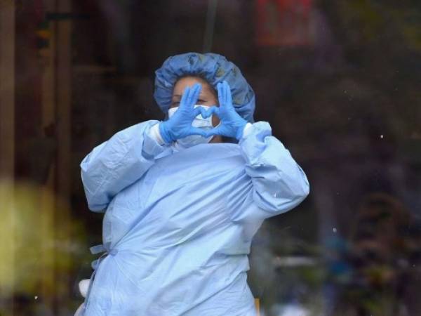 Un trabajador de salud forma un corazón a través de una ventana en un centro médico. Foto: AFP.