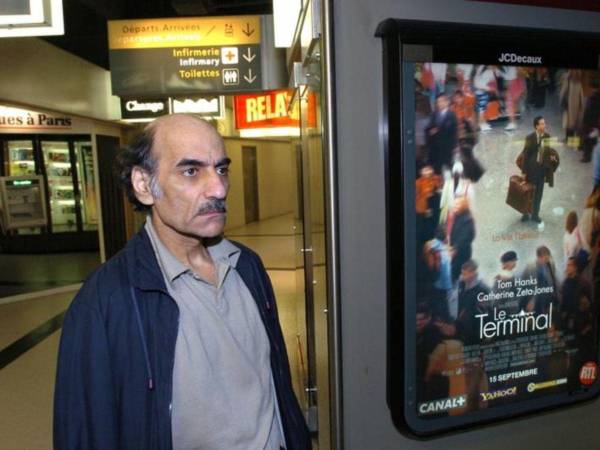 Mehran Karimi Naser junto al poster de la película “La Terminal” de Steven Spielberg inspirada en su vida.