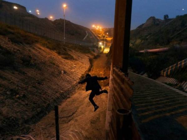 En esta fotografía de archivo del viernes 21 de diciembre de 2018, un joven hondureño salta a territorio estadounidense desde la valla fronteriza en Tijuana, México.