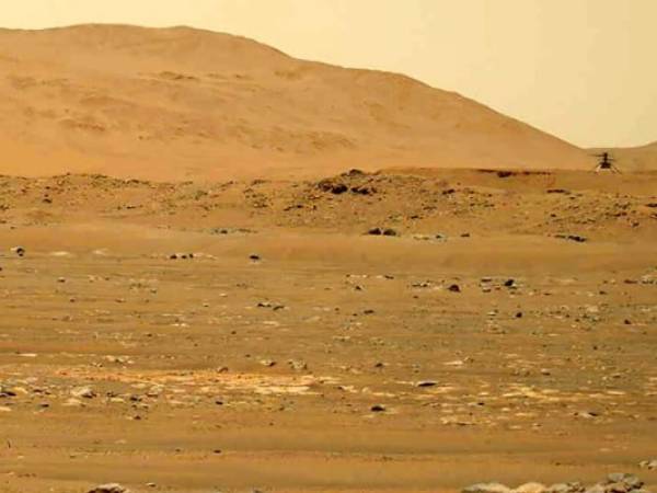 En esta imagen del 30 de abril de 2021 tomada por la sonda Mars Perseverance y difundida por la NASA, se ve al helicóptero Mars Ingenuity, a la derecha, sobrevolando la superficie del planeta.