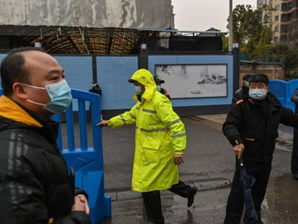 Los guardias se paran en una entrada mientras los miembros del equipo de la Organización Mundial de la Salud (OMS), que investigan los orígenes del coronavirus covid-19, llegan al mercado mayorista cerrado de Huanan Seafood en Wuhan, provincia central de Hubei en China, el 31 de enero de 2021.