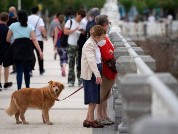 Dos ancianas pasean a un perro mientras miran el mar desde una explanada a lo largo de la playa de La Concha en San Sebastián, el 9 de mayo de 2021. España ha levantado el estado de emergencia vigente desde octubre de 2020 para combatir la pandemia. Foto: AFP