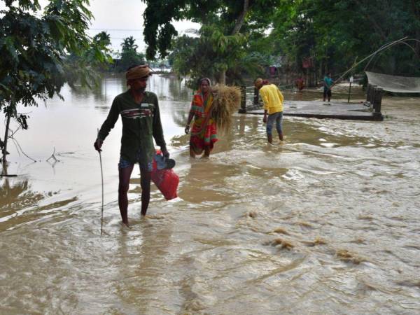 Los aldeanos caminan a través de las aguas de la inundación después de las fuertes lluvias en el distrito de Hojai, estado de Assam, el 21 de mayo de 2022.