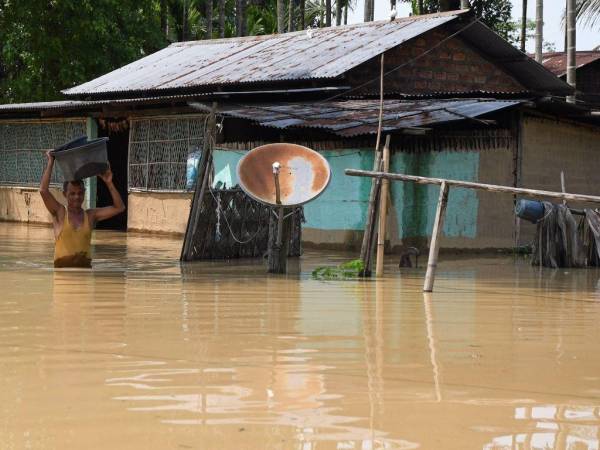 Un hombre lleva sus pertenencias a través de un área inundada después de fuertes lluvias en el distrito de Morigaon del estado indio de Assam el 22 de mayo de 2022.