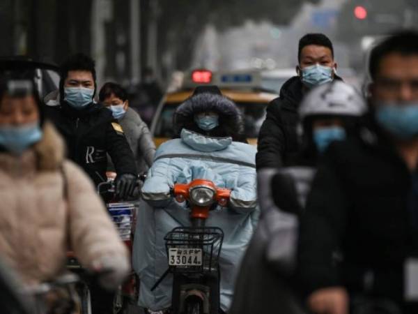 Viajeros vestidos con máscaras pasan por The Jade Boutique Hotel, donde los miembros del equipo de la Organización Mundial de la Salud (OMS) que investigan los orígenes de la pandemia del coronavirus covid-19 deben completar su cuarentena, en Wuhan, provincia central de Hubei en China, el 28 de enero. 2021. Foto: AFP