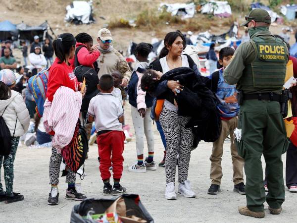 Varios migrantes esperan bajo la mirada atenta de un guardia. Foto de referencia.