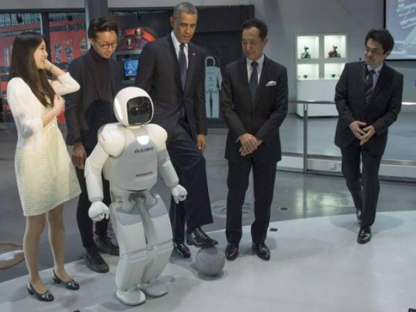 US President Barack Obama (C) positions a football as he talks with Honda's humanoid robot ASIMO (R), an acronym for Advanced Step in Innovative MObility, student Nao Yamamoto (L), student Iida Satoru (2nd L) and chief executive director of the Miraikan Museum, Mamoru Mohri (2nd R), as he tours the Miraikan Science Expo in Tokyo on April 24, 2014. Obama earlier vowed to defend Japan if China attacks over a tense territorial dispute, but also urged Beijing to help stop North Korea from forging ahead with its 'dangerous' nuclear programme. AFP PHOTO / Jim WATSON