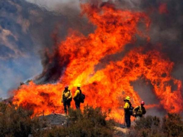 Varios bomberos observan un incendio el domingo. Foto AP.