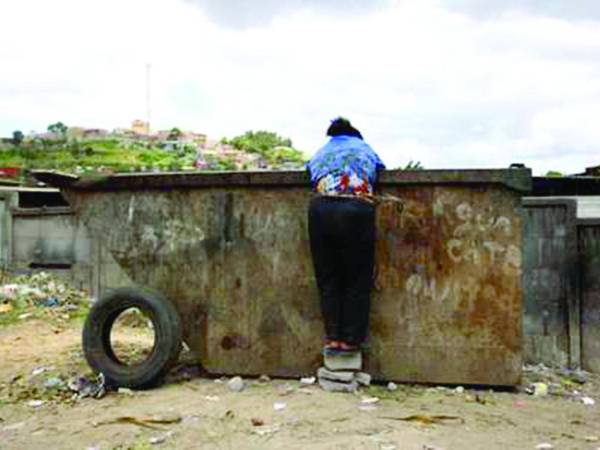 Una persona en situación de calle busca entre la basura alimento o cualquier objeto que pueda vender para ganar unos pocos lempiras.