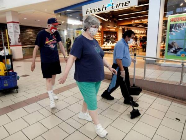 Una pareja con mascarillas camina frente a un trabajador de limpieza en el centro comercial Gateway, en Lincoln, Nebraska, el viernes 1 de mayo de 2020. (AP Foto/Nati Harnik)