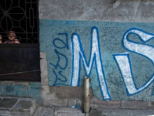 Un niño mira desde detrás de la puerta de su casa, cubierto con graffiti de pandillas Mara Salvatrucha, en Soyapango, El Salvador. Procuradores generales en Centroamérica expresan preocupación.