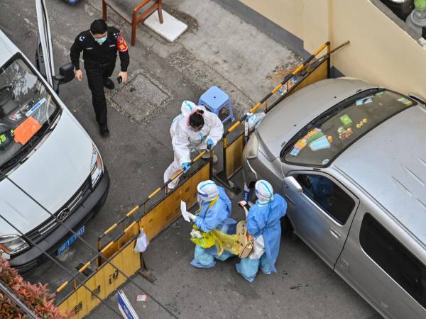 Trabajadores sanitarios con equipo de protección personal (EPP), se sitúan en un punto de control junto a un barrio durante un cierre de COVID-19 en el distrito de Jing’an, Shanghái.