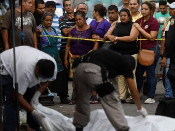 Investigadores policiales trabajan en la escena del crimen donde cinco vendedores del mercado y un guardia de seguridad privado fueron asesinados durante una supuesta confrontación de pandillas en San Salvador. Foto: Agencia AFP.