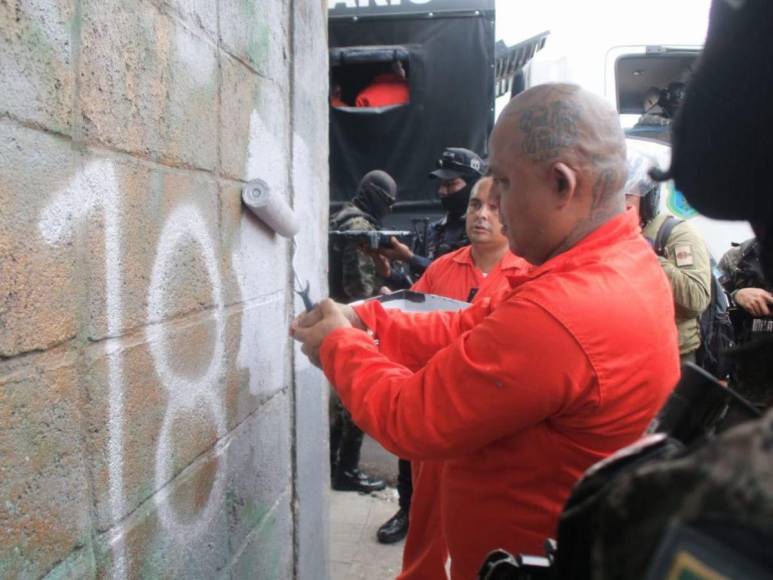 De overol naranja y grilletes, reclusos borran “placazos” de maras y pandillas en la capital