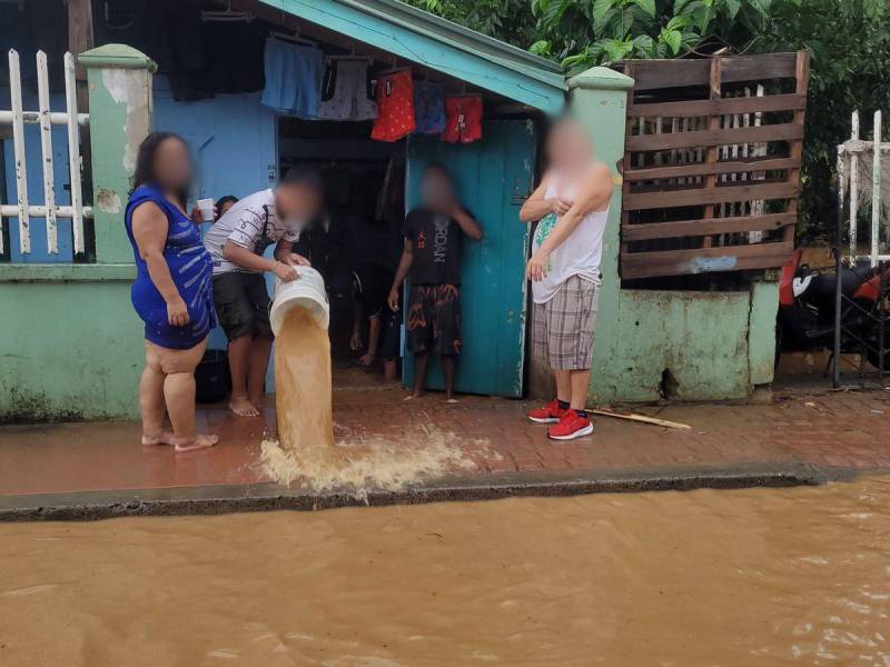 Con baldes, hondureños intentan sacar el agua que ha alcanzado el nivel de la acera de las calles cerca de sus viviendas.